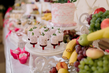 A table with a variety of desserts and fruits, including a pink cake. The desserts are served in small cups and the fruits are displayed on a platter. The table is set up for a party or gathering