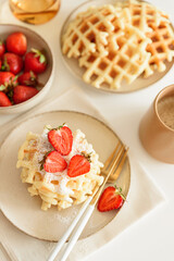 Belgian waffles with strawberries and powdered sugar on white table. Summer food concept. Soft focus