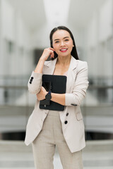 Fototapeta premium Confident Businesswoman Holding Tablet in Modern Office. A confident businesswoman stands in a modern office space holding a tablet, symbolizing leadership, professionalism, and career success.