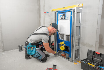 In-wall toilet system assembly. Plumber does anchoring the supporting structure to the floor.