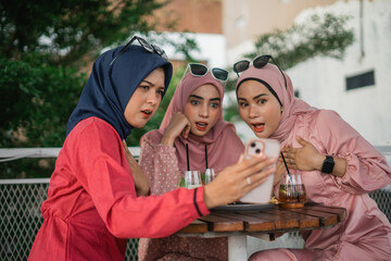 Three friends excitedly watching a video on their phone at a caf