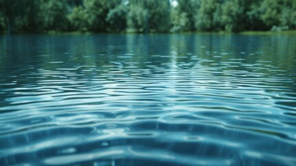 Fototapeta premium Close-up of calm blue water with ripples and a blurred background of green trees.