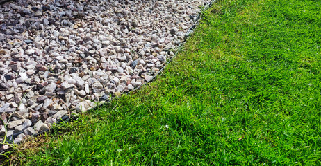 Close-up of a garden area with a well-maintained green lawn adjacent to a decorative stone pathway. Contrast between grass and rocks adds texture and visual interest.
