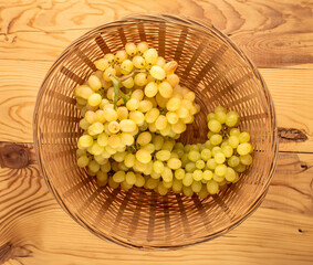 One bunch of ripe white grapes in a straw plate on a wooden table, macro, top view.