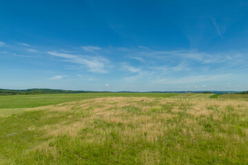 A serene landscape featuring a vast green field under a clear blue sky with wispy clouds. This tranquil scenery is perfect for nature lovers and outdoor enthusiasts.