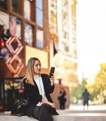 Fototapeta premium Coffee break in a public city spot: beautiful and relaxed blonde latina executive with coffee cup using the phone