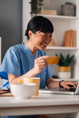 Asian nurse in scrubs making an online purchase with a credit card