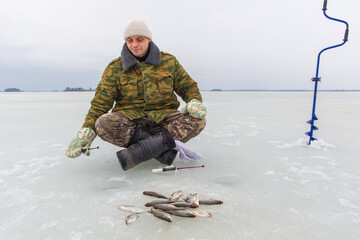 Man. European man, 45 years old, fishing on the ice of a lake. Fresh fish lies on ice.