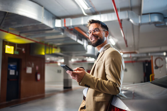 Portrait of businessman using smartphone while standing near his car in underground garage.