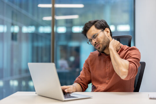 Man using laptop in office shows neck pain and discomfort, representing challenges related to prolonged computer work. Image captures workplace strain and need for ergonomic support during tasks.