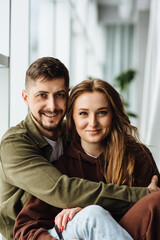 Portrait of happy young couple smiling and hugging showing love affection. Beautiful and in love man and woman spend weekend together at home. Young adult boy and girl having fun and looking at camera