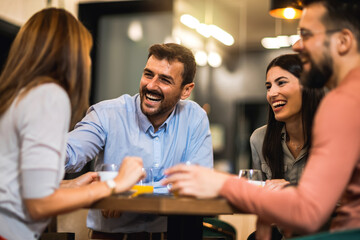 Group of friends hanging out at the cafe. The guy takes the lead in the conversation. Drinking orange juice and coffee.