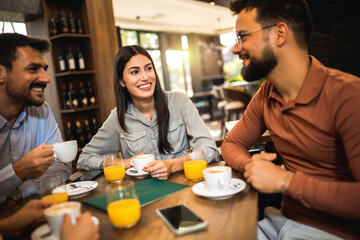 Group of friends laughing together at the coffee shop. They drink orange juice and hang out...