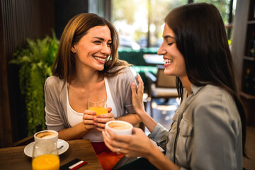 Two girl friends met at the coffee shop to hang out, gossip and talk to each other. They are drinking coffee and orange juice.