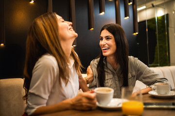 Two girl best friends having out at the restaurant. Drinking coffee and orange juice. They gossip, laugh and have fun time.