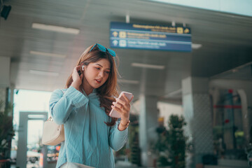 A traveler intently focused on her smartphone while situated in a busy airport environment