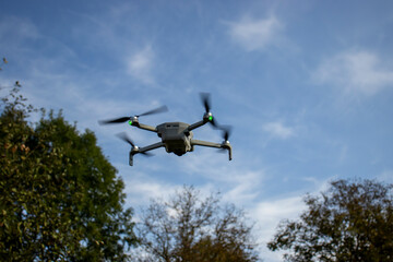 Drone flying in a clear sky over trees. Green and black quadcopter in action, surrounded by nature. Daytime, outdoor aerial photography concept.