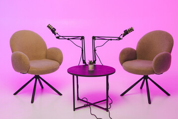 Cozy podcast setup with two chairs and microphones against a vibrant pink background