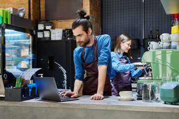 Two cafe workers working together behind counter, at coffee shop