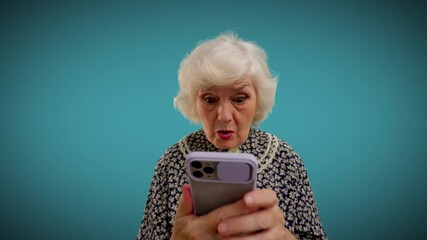 Shocked granny reading message on phone against blue background, amazing news