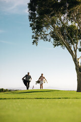 Wide angle shot of a man and woman walking together towards the green on a golf course carrying golf bags © Jacob Lund