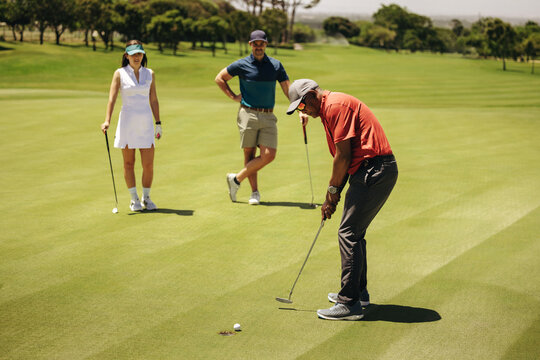 Golf players putting on the green as team members watch during a competitive game