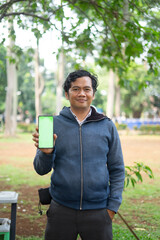 Fototapeta premium Southeast Asian man showing something on his smartphone with a green screen, perfect for customizable content