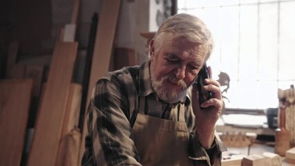 Portrait of bearded Caucasian man talking on smartphone with someone. Smiling while looking down. Enjoying communication. Concept of remote communication. Male taking break from work. - Powered by Adobe