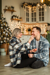 a couple in love in checkered sweaters look at each other against the backdrop of lights in the kitchen of their home. Christmas family holiday 