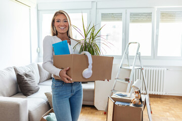 Happy woman carrying her belongings while relocating into new apartment. Young woman holding a box...