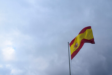 Bandera de España ondeando al viento en mástil sobre cielo nublado