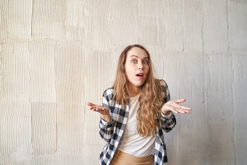 Obraz premium Confused woman shrugging against textured wall - expressions of uncertainty and curiosity in casual checkered shirt scene.