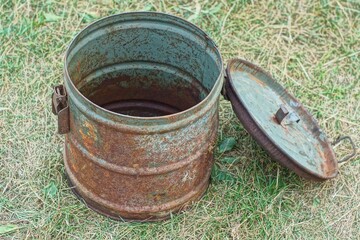 Fototapeta premium one round rusty retro iron dirty empty open old with lid industrial with handle and latches large container stands on green day outside 