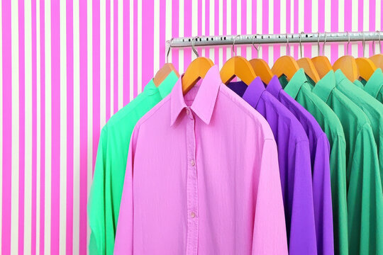 Colorful shirts on hangers against a pink striped background