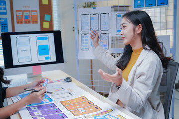 Ui/ux designers are working together in the office. They are discussing the mobile app interface design using the wireframe display on the table