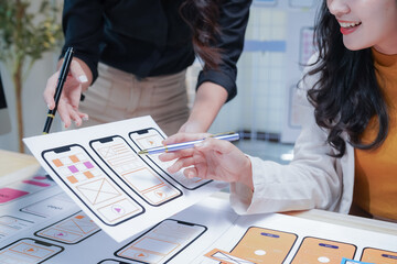 Two female ui/ux designers are working together in the office, discussing over a mobile application interface wireframe design