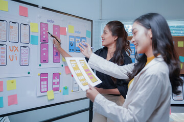 Two asian female ui/ux designers are discussing the user interface of a mobile application, working together in the office