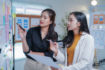 Two asian ui/ux web designers are reviewing mobile app interface designs and the user journey of their new mobile application