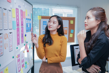 Two asian female ui/ux designers are discussing over mobile app interface wireframe design...