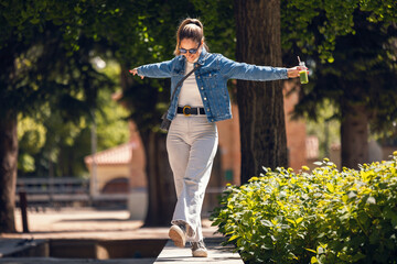 Happy beautiful woman dancing and walking while drinking detox juice across the park