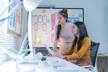 Two asian female ui/ux designers are discussing over new mobile application in modern office, working together on a project