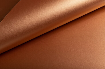 Copper metallic texture with glossy folds and reflective sheen. Smooth designer paper featuring an abstract pattern with elegant curves. Soft light and subtle shadows highlight the
