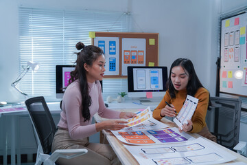 Two female ui/ux designers are working together in the office, discussing over new mobile application interface wireframe design