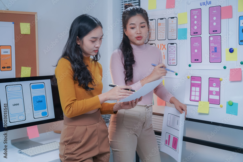 Wall mural two female ui/ux designers are discussing user interface design for a mobile application. using a wh