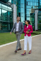 Handsome man and beautiful woman as business partners walking and exchange opinions in front off glass building exterior. Smiling business man and woman on break ,walking around and talk.

