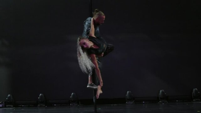 Circus performers, a guy and a girl, are doing tricks on the pole