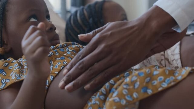 Close up shot of unknown doctor palpating abdomen of African American little girl during medical examination at kids clinic, elder sister lying in background