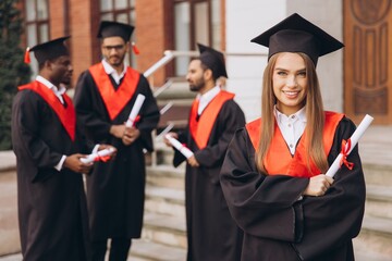Joyful Young Woman Celebrating Graduation with Friends in Academic Gowns Outdoors