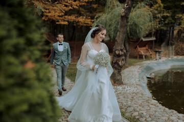 A man and woman are standing on a bridge, with the woman wearing a wedding dress. The man is touching the woman's face, and they are both smiling. Scene is happy and romantic