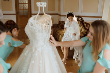 Naklejka premium A bride is getting ready for her wedding and her bridesmaids are helping her. One of the bridesmaids is holding a dress up to the bride's face